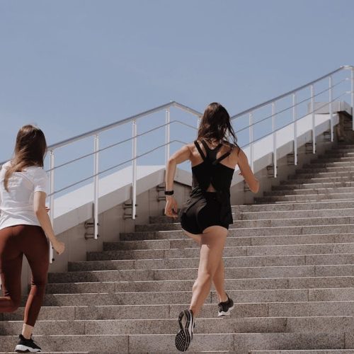 Two women running up stairs outdoors, embodying fitness and wellness.