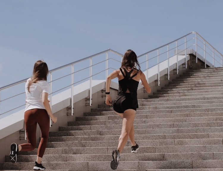 Two women running up stairs outdoors, embodying fitness and wellness.