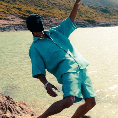 Man in teal shirt and shorts by the ocean