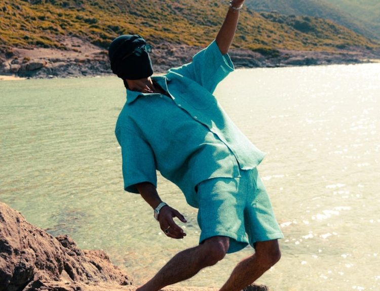 Man in teal shirt and shorts by the ocean