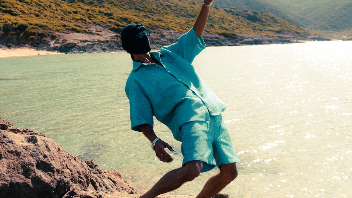 Man in teal shirt and shorts by the ocean